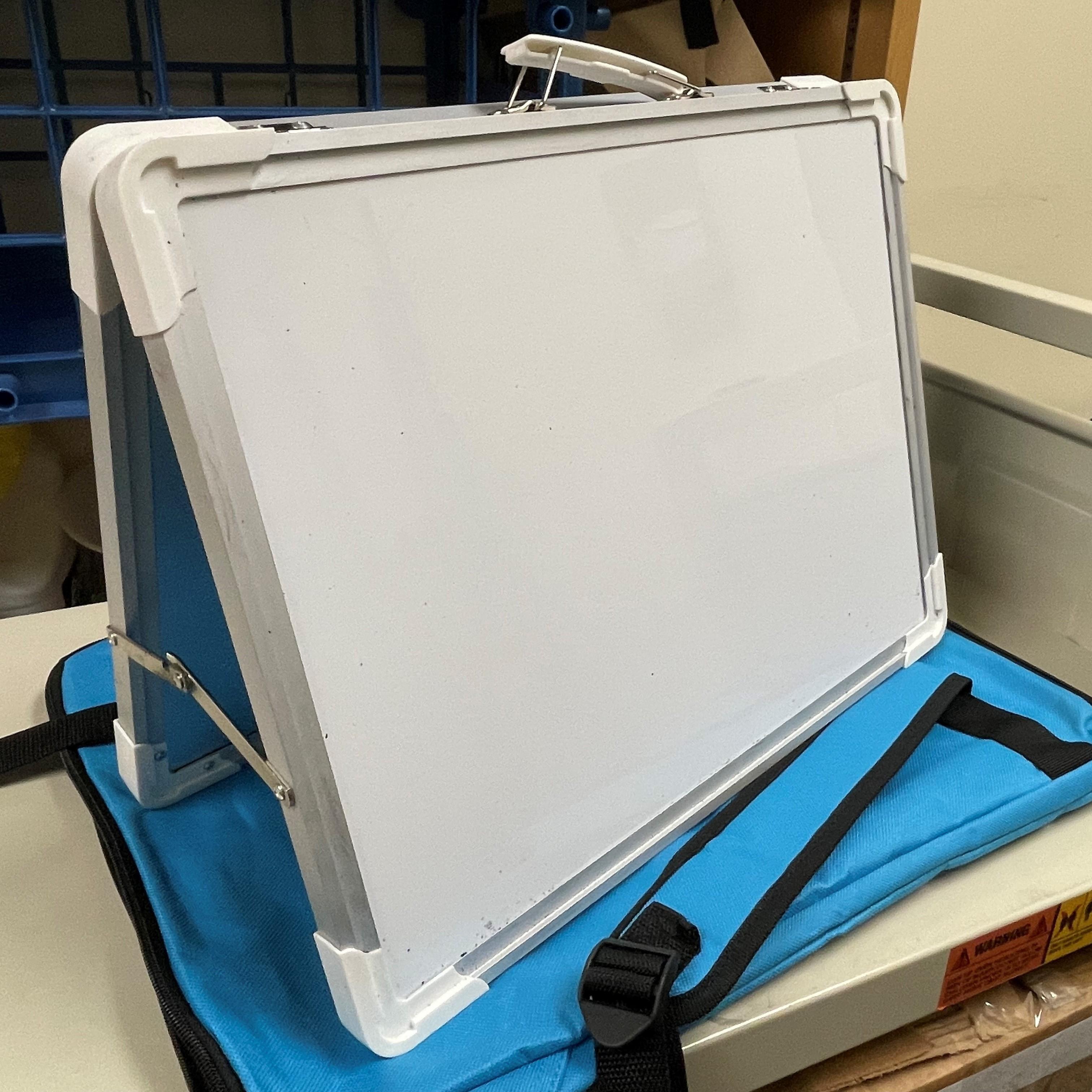 Photo of one of the small whiteboards with its stand opened up, sitting on its turquoise backpack.